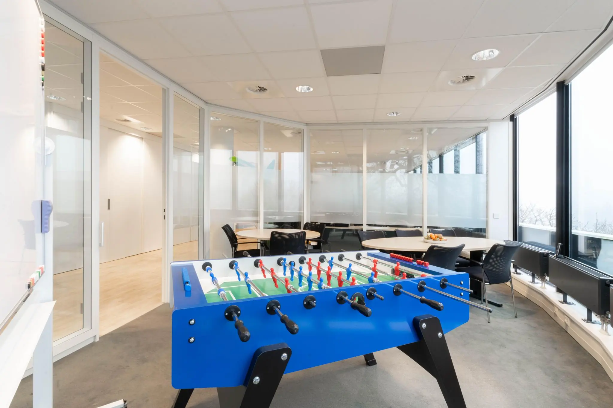 Moderne kantoorruimte aan de 1e Hogeweg met glazen wanden, vergadertafels en een blauw tafelvoetbalspel.